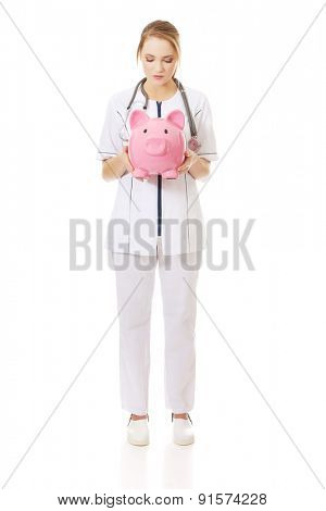 Young beautiful female doctor holding a piggybank.