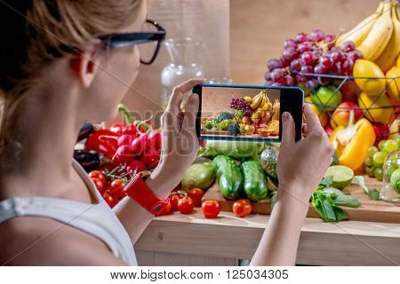 Female food photographer photographing with smartphone fresh fruits and vegetables