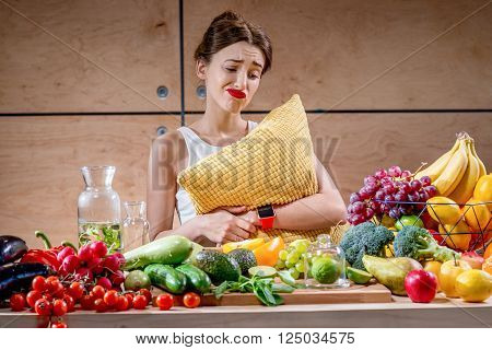 Sad woman with pillow watching reluctantly at the fuits and vegetables in the morning or in the evening before sleeping. Diet and healthy food concept