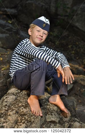 boy in a frock and garrison cap sitting on the stone with barefooted