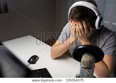 technology, gaming, entertainment, let's play and people concept - close up of sad young man in headset with pc computer playing game at home and streaming playthrough or walkthrough video