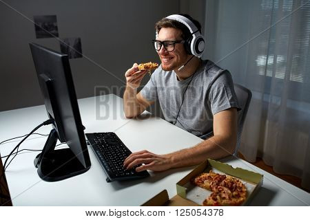 technology, gaming, entertainment, let's play and people concept - happy young man in headset with pc computer eating pizza while playing game at home and streaming playthrough or walkthrough video
