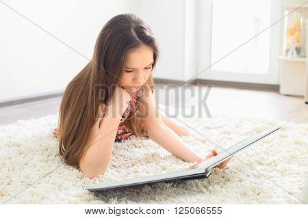 Charming little girl reading book on white carpet