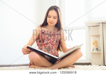 Charming little girl reading book on white carpet