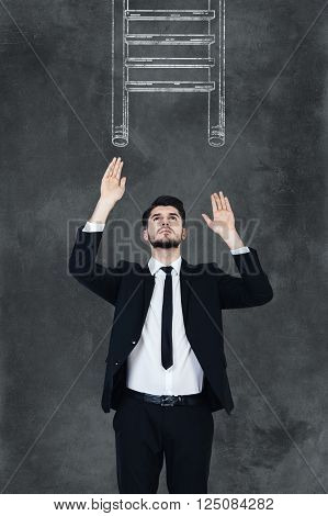 Helping ledder. Handsome young man in formalwear stretching out his hands and looking up while standing against chalkboard with drawing ledder on it