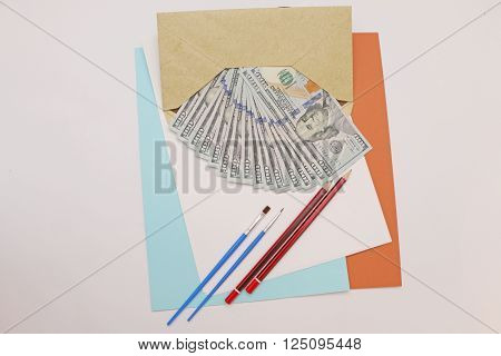 dollar bills folded in an envelope with paper and beside it lay pipes and pencils to color in.