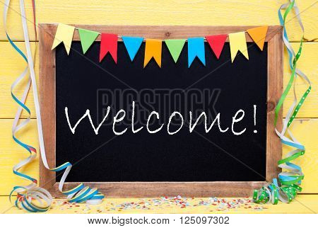 Chalkboard With English Text Welcome. Party Decoration Like Streamer, Confetti And Bunting Flags. Yellow Wooden Background With Vintage, Retro Or Rustic Syle