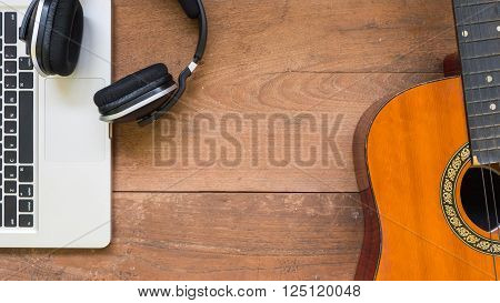 Top view workspace with laptop, headphone and acoustic guitar on wooden table background.Free space for your text.