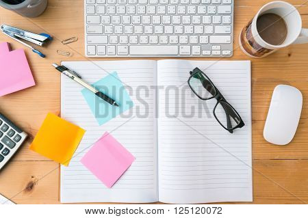 Top view on opened notebooksticky note cup of coffee keyboard other equipment on wooden office desk.