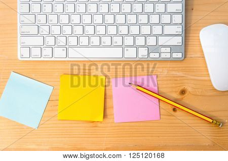 Top view of colorful sticky notes pencil keyboard and mouse on wooden table background.
