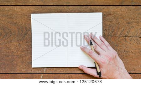 Man hands with pen writing on empty notepad over a wooden table.