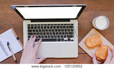 Laptop, notebook, pen and breakfast on wooden table background.
