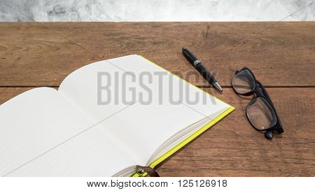 Blank notebook with pen and glasses on a wooden table.
