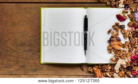 Top view workspace with blank notebook, pen and dried flowers on wooden table background .