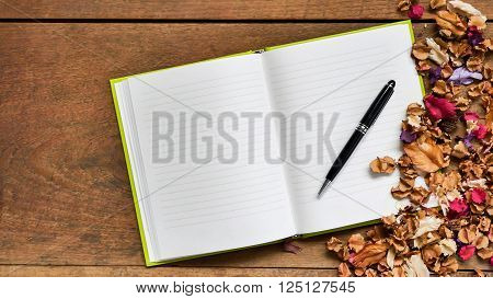 Top view workspace with blank notebook, pen and dried flowers on wooden table background .