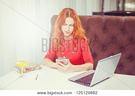 Happy entrepreneur working with a phone and laptop in a coffee shop.