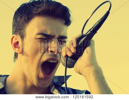 Young rock singer singing in vocal microphone with great passion. Warm yellow film collor.