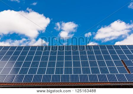Several rowss of solar panels on roof with blue sky and white clouds