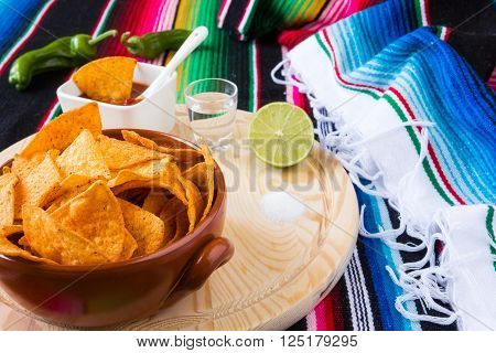 Nachos chips tequila lime and salt over a chopping board with a colored poncho background
