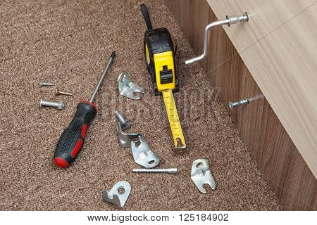 Hand tools for assembling furniture at home, Phillips screwdriver measuring tape, metal brackets, screws and Allen key.