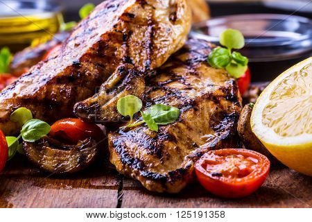 Grilled chicken breast in different variations with cherry tomatoes mushrooms herbs cut lemon on a wooden board or grill pan. Traditional cuisine. Grill kitchen