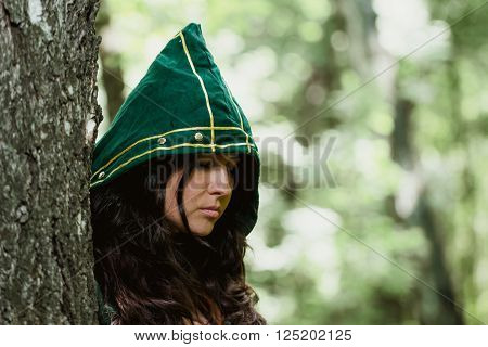 Staging photo of beautiful woman in fantasy suit with hood in forest