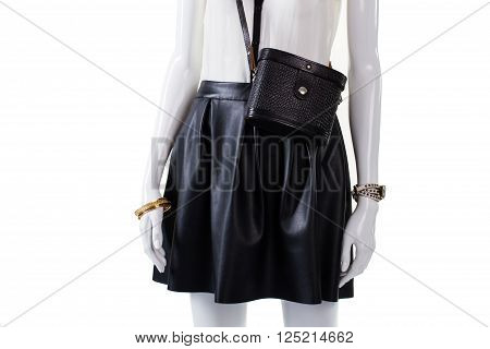Purse and skirt on mannequin. Retro handbag with leather skirt. Woman's fashionable dark skirt. Gold bracelet and black bag.