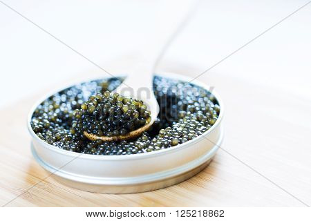 close-up view of metal tin with black sturgeon caviar and wooden spoon on it