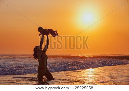 Happy family swimming fun on sea beach - mother tossing up baby son into mid air catching on sunset sky sun background Parents outdoor activity child lifestyle on summer vacation in tropical island