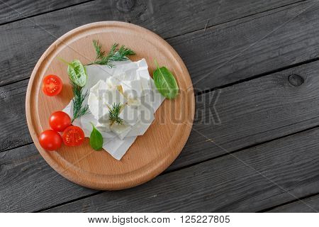 Sliced feta cheese with dill, cherry tomatoes and spinach leaves on wooden table on a wooden board, top view with copy space
