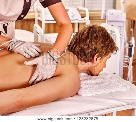 Handsome serious man  receiving electric massage at beauty salon. Beautician wearing electricity gloves. 