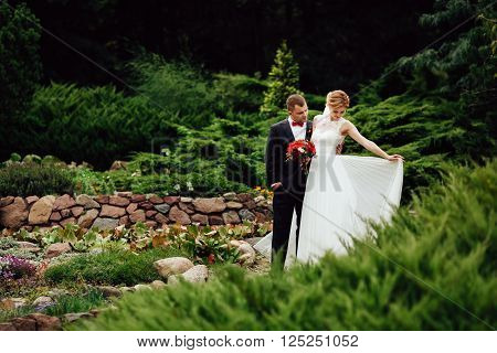 elegant stylish groom with his happy gorgeous blonde bride on the background of trees in the autumn park. Blank space on left