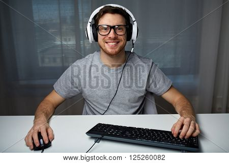 technology, gaming, entertainment, let's play and people concept - happy smiling young man in eyeglasses with headset playing computer game at home and streaming playthrough or walkthrough video