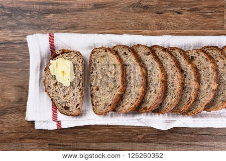 Top view of a sliced loaf of multi-grain bread on a towel, one slice is buttered.