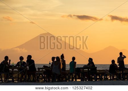 Tourists in the restaurant on Gili Travangan island enjoying evening sunset view on Gunung Batur volcano on Bali, Indonesia.