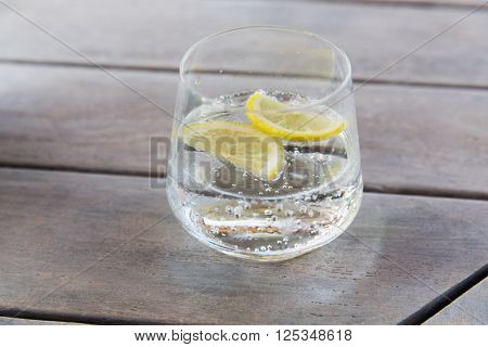 drink and refreshment concept - glass of sparkling water with lemon slices on table