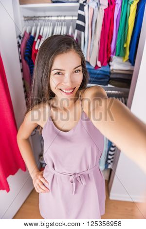 Changing room Asian woman taking selfie picture of her outfit. Young ethnic girl trying on a fashion dress taking a photo of herself in the fitting room or at home in her bedroom walk-in closet.