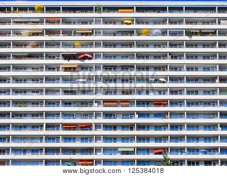 Wall of tall residential building, background of balconies with colorfull umbrellas and awnings.
