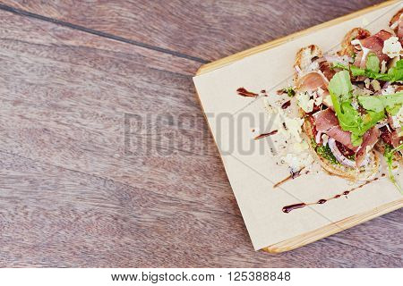 Cropped overhead view of a delicious gourmet bruschetta with fresh parma ham, crsip rocket leaves and petso, presented on a rustic wooden table
