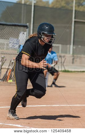 Strong softball player in black uniform running to first.
