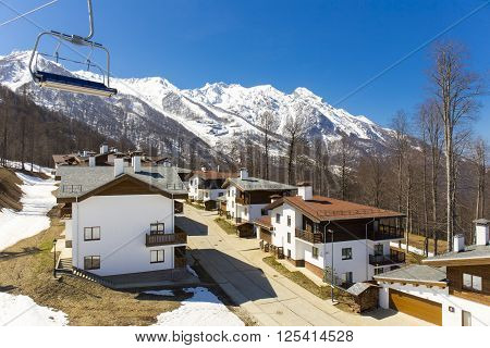 ROSA KHUTOR, RUSSIA - APRIL 01, 2016: Mountain ski resort Rosa Khutor with cottages on snowy mountains background