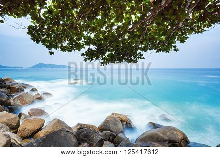 Long exposure of Kalim Beach in Phuket with boulders sea and deciduous tree