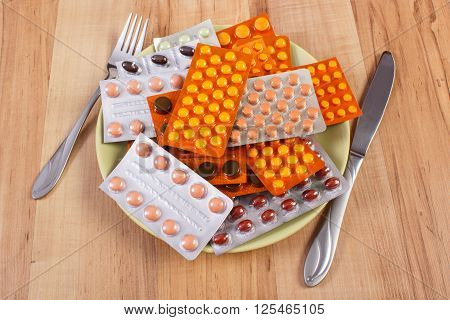 Blisters of colorful medical pills capsules or supplements on plate and fork with knife concept of treatment and health care