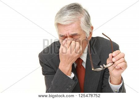 studio shot of senior Japanese businessman suffers from Asthenopia
