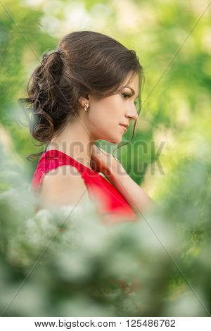 Portrait of Beautiful young brunette woman in park surrounded of white flowers with white flowers  on a warm summer day