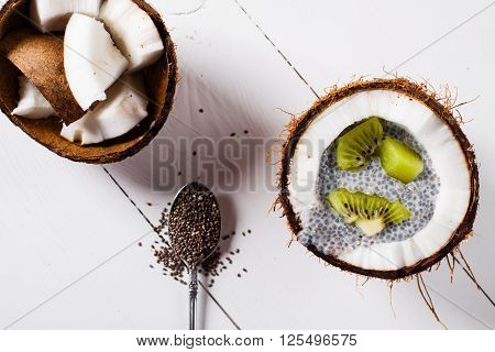 Chia seeds pudding with kiwi fruits in the shell of a coconut on white wooden background. Flat lay.