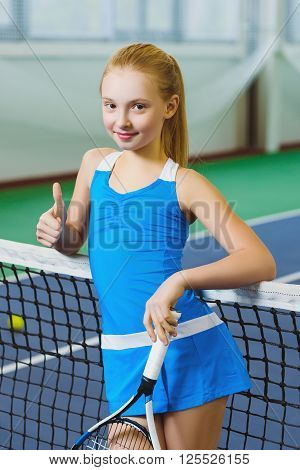 Cute girl playing tennis and posing or show thumb up  in court indoor.