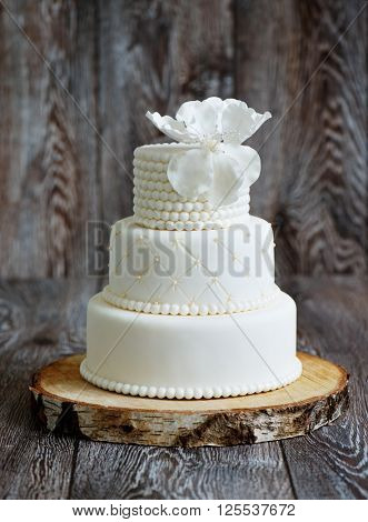 Wedding cake covered with white fondant, decorated with beads and hand-made flower on top