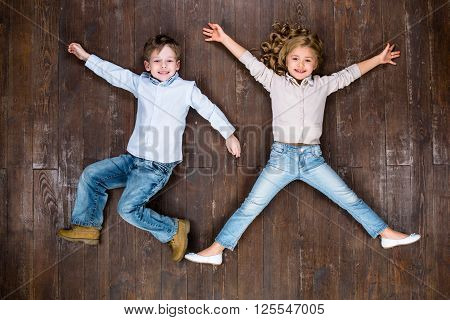 Happy children. Top view creative photo of little boy and girl on vintage brown wooden floor. Children looking at camera and smiling