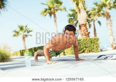 Handsome man doing push ups on the beach.